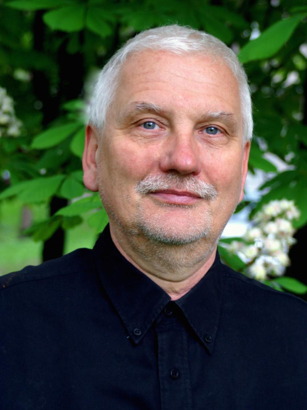 Pianista Michał Korzistka w siwych włosach i czarnej koszuli pozuje na tle zieleni